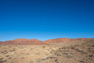 Weite W&uuml;stenlandschaft unter klarem Himmel, mit felsigem Gel&auml;nde und majest&auml;tischen Bergen in der Ferne.