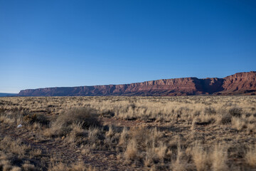  Die Szenerie wird von hoch aufragenden Tafelbergen und einer fernen Bergkette dominiert, die in die warmen Farbtöne des amerikanischen Südwestens getaucht sind. 