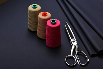 Dark navy blue, 180s quality cashmere suiting fabric with sewing scissors and thread, on the table of fashion design studio.