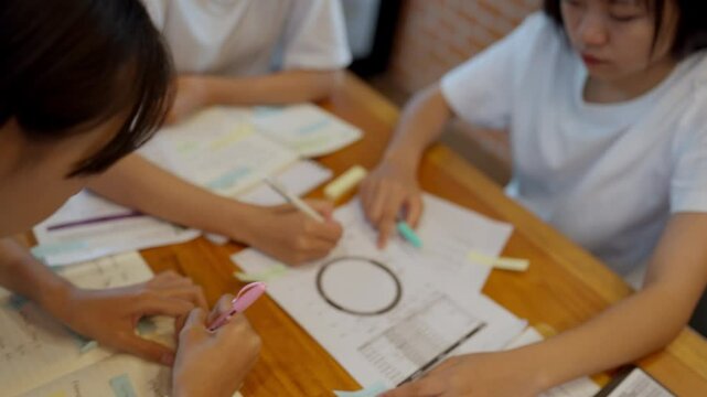 A group of people are sitting around a table with papers and markers. They are working on a project together, and the mood of the image is collaborative and focused