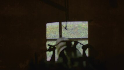 A blurred silhouette of a machine gun pointed at the embrasure in the wall. Close-up shot of a machine gun in a loophole.