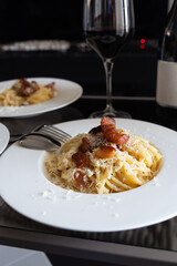 Fototapeta premium Close up of plate of closeup carbonara spaghetti topped with grilled bacon with red wine in background.