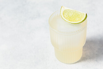 Refreshing lime cocktails on white table. Glass of citrus hard seltzer with ice cube and fresh lime...