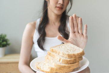 Gluten allergy, asian young woman hand push out, refusing to eat white bread slice on plate in...