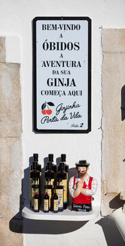 Obidos, Portugal - 17 August 2021: Welcome to Obidos white board. Several bottles of ginja and a ze povinho figurine displayed. Ginja is a typical portuguese liquor