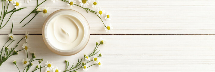 Natural skincare cream in jar surrounded by small white flowers and green leaves on wooden background