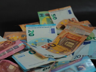 Scattered euro bills on a black background. Various denominations and security details are clearly visible in the macro view