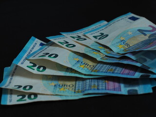 Close-up of 20-euro banknotes on a black background. Details of the banknotes are clearly visible, including paper texture, watermarks and security features.