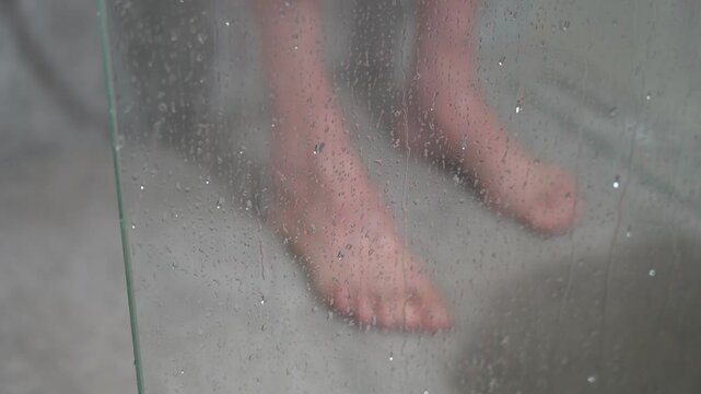 Elderly man taking a shower, view through the fogged glass of the shower stall