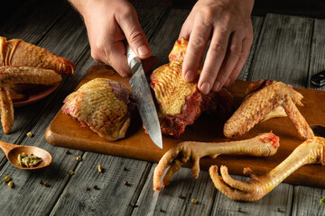 Hands are skillfully cutting raw poultry on a wooden board, surrounded by fresh chicken parts and spices, showcasing a culinary preparation process in a rustic kitchen setting