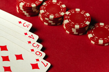 A setup for a card game features several red poker chips stacked next to a hand of playing cards showing diamonds straight flush. The table surface is bright and inviting, enhancing gaming atmosphere