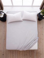 Double bed with two white pillows, covered with a gray fitted sheet with an elastic band and two black bedside tables. The corner of the mattress is visible. Top view photo. Suitable for mockups.