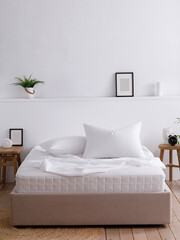 Modern bedroom decorated with handmade furniture. Double bed with two pillows and white sheets elegantly draped over the mattress. A part of the mattress is visible. Front view. Suitable for mockup.