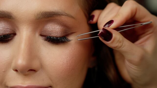 Professional makeup artist applying false eyelashes with precision tweezers, carefully working on client's eye during delicate beauty salon grooming procedure