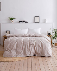 Double bed with two handcrafted bedside tables in a bedroom with a modern interior and wooden floor. Fluffy duvet and two white pillows is on the bed. Vertical front view photo. Suitable for mockup