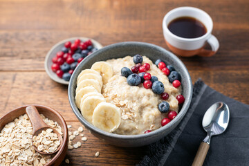 Oatmeal bowl with berries and banana on a wooden table background