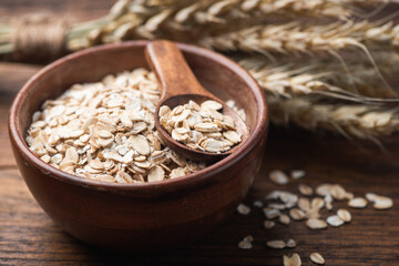Oatmeal, dry rolled oat flakes in wooden bowl, closeup view. Dietary fiber