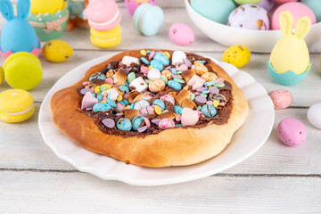Sweet Easter dessert pizza, with chocolate paste topping, marshmallow and Easter chocolate eggs, snack for Easter holiday kids party, with festive decorations, colorful eggs and bunny rabbits