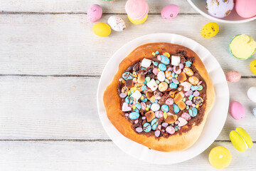 Sweet Easter dessert pizza, with chocolate paste topping, marshmallow and Easter chocolate eggs, snack for Easter holiday kids party, with festive decorations, colorful eggs and bunny rabbits
