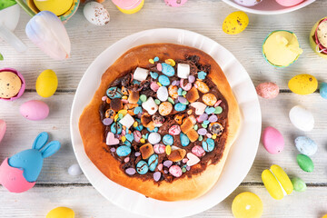 Sweet Easter dessert pizza, with chocolate paste topping, marshmallow and Easter chocolate eggs, snack for Easter holiday kids party, with festive decorations, colorful eggs and bunny rabbits