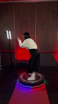A woman poses on a 360-degree photo booth platform with LED lights, engaging in an interactive video experience at an event.