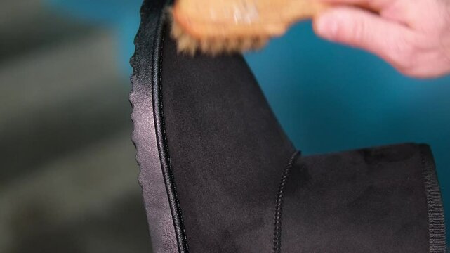 Topic care and brushing warm shoes expertly with small brush in workshop. Professional cleaning of nubuck shoes, suede autumn boots black, winter care and cleaning footwear. Boot maintenance studio. 