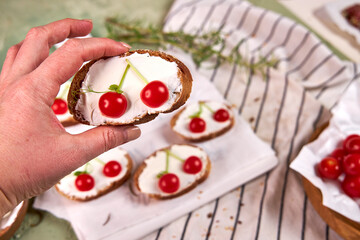 Creative tartines with white cheese and tomato cherries rest on a white board on a green table and a striped napkin