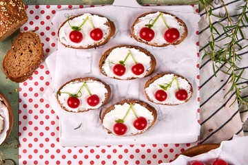 Creative tartines with white cheese and tomato cherries rest on a white board on a green table and a striped napkin