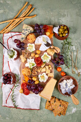 creative serving of cheese board with different cheeses, pistachio honey, fruits, nuts, white wine and floral decoration on green background