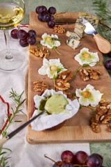 creative cheese board serving with soft mold cheese, pistachio honey, white wine and floral decoration on green background