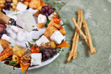 oval dish with a wreath of cheese and meat appetizers with vegetables on a green table, creative serving view from above