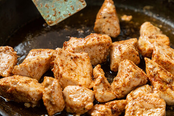 Chicken fillet pieces are fried in a frying pan in sauce and spices