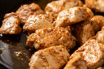 Chicken fillet pieces are fried in a frying pan in sauce and spices.
