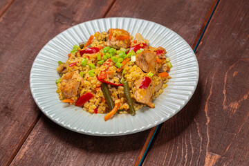 On a wooden table in a plate there are vegetables stewed with bulgur