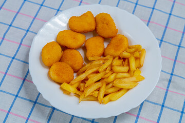 French fries and golden nuggets in a plate on a white checkered tablecloth