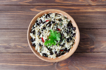 Traditional Costa Rican dish - Gallopinto. Black beans and rice stewed with onions, garlic, cilantro in a ceramic bowl on a wooden table. Selective focus. Horizontal orientation. Top view . Copy space