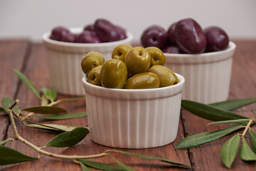 Black and green olives in round bowls, on a rustic wooden background with olive leaves
