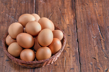 Raw brown eggs arranged in a basket with a rustic wooden background