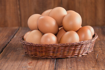 Raw brown eggs arranged in a basket with a rustic wooden background