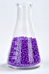 Purple masterbatch granules in Erlenmeyer flask isolated on white background, color pigment carrier...