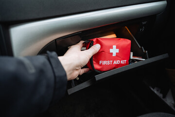 A person is meticulously retrieving a first aid kit from the glove box of their car, underscoring...