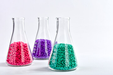 Red, purple and turquoise masterbatch granules in Erlenmeyer flask isolated on white background,...