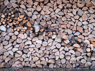 A neatly stacked pile of firewood, showing various sizes and textures of cut logs. The natural wood patterns and earthy tones create a rustic and warm aesthetic, symbolizing preparation for winter.