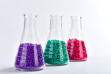 Red, purple and turquoise masterbatch granules in Erlenmeyer flask isolated on white background,...