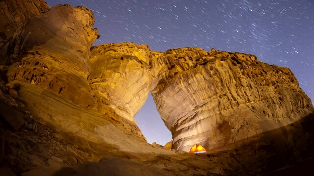 Time lapse of night stars motion while camping tent at bottle shape rock formation near elephant rock in Alula, Madinah, Saudi Arabia