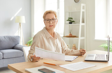Concentrated elderly businesswoman focused on working with documents and a laptop at home office....