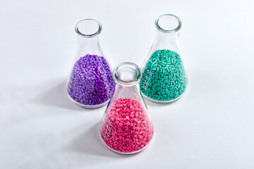 Red, purple and turquoise masterbatch granules in Erlenmeyer flask isolated on white background,...
