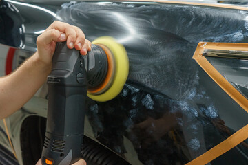 Taking care of the car's appearance. The master polishes the front fender of a black car.