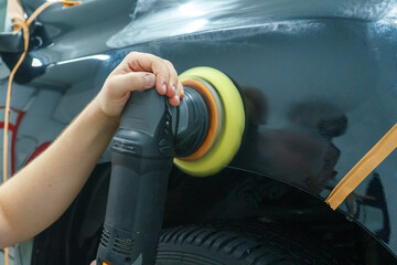 Taking care of the car's appearance. The master polishes the front fender of a black car.