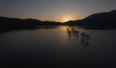 sunset on a lake with small trees in the water